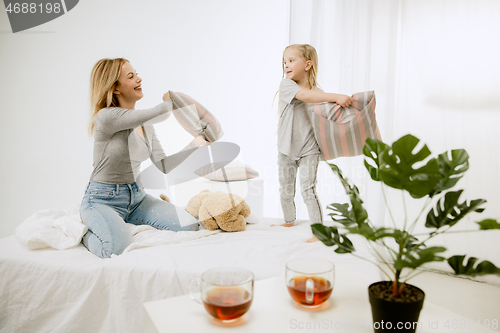 Image of Young mother and her little daughter hugging and kissing on bed