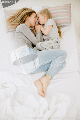 Image of Young mother and her little daughter hugging and kissing on bed