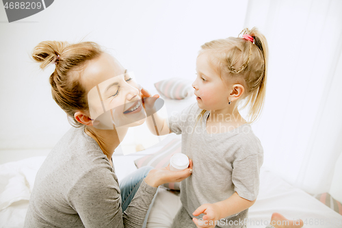 Image of Young mother and her little daughter hugging and kissing on bed