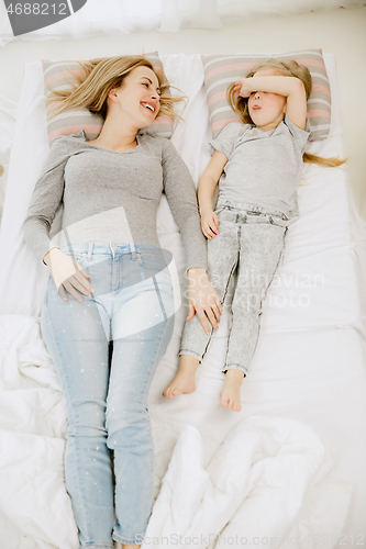 Image of Young mother and her little daughter hugging and kissing on bed