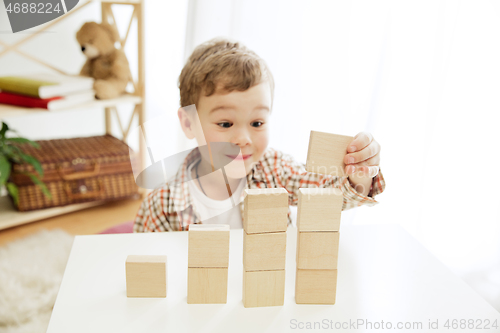 Image of Little child sitting on the floor. Pretty boy palying with wooden cubes at home