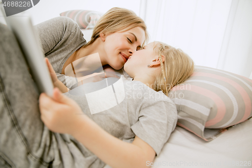 Image of Young mother and her little daughter hugging and kissing on bed