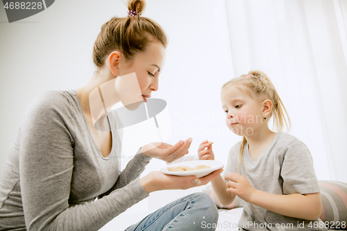 Image of Young mother and her little daughter hugging and kissing on bed