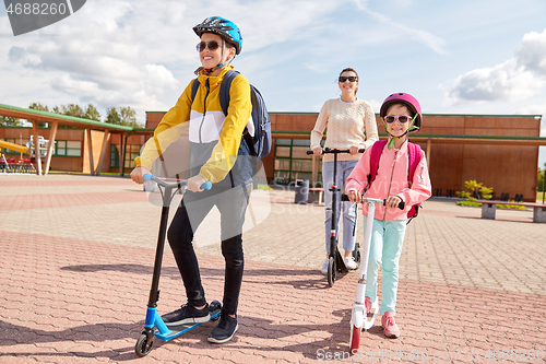 Image of happy school children with mother riding scooters