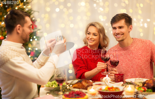 Image of happy friends photographing at christmas dinner