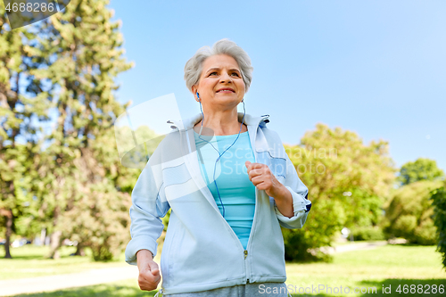Image of senior woman with earphones running in summer park