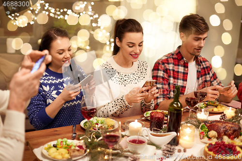 Image of friends with smartphones having christmas dinner