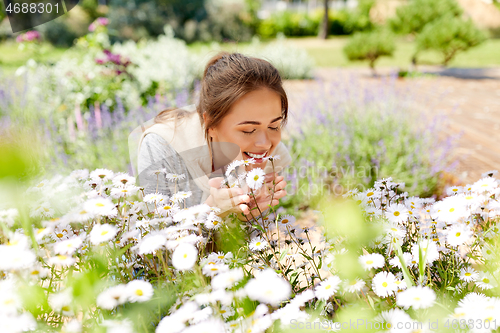 Image of happy woman smelling chamomile flowers in garden