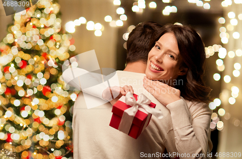 Image of happy couple with christmas gift hugging at home