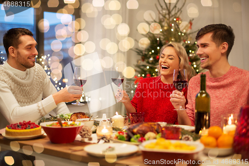 Image of happy friends drinking red wine at christmas party