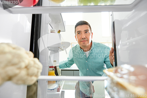 Image of man looking for food in fridge at kitchen