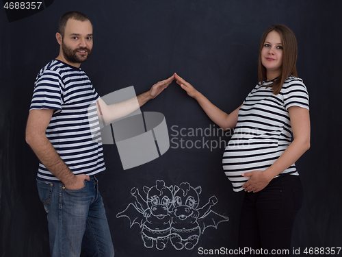 Image of pregnant couple drawing their imaginations on chalk board