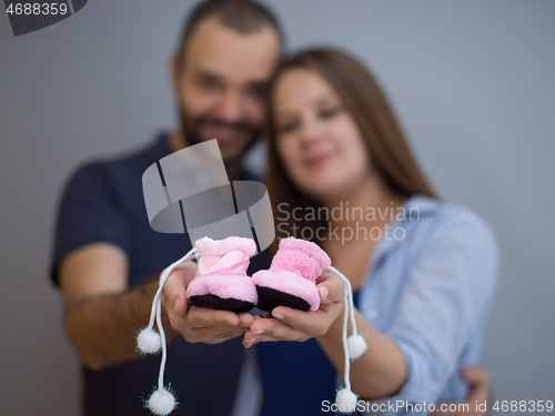 Image of pregnant couple holding newborn baby shoes