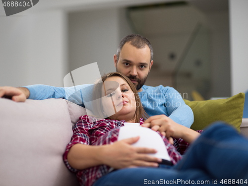 Image of young pregnant couple relaxing on sofa