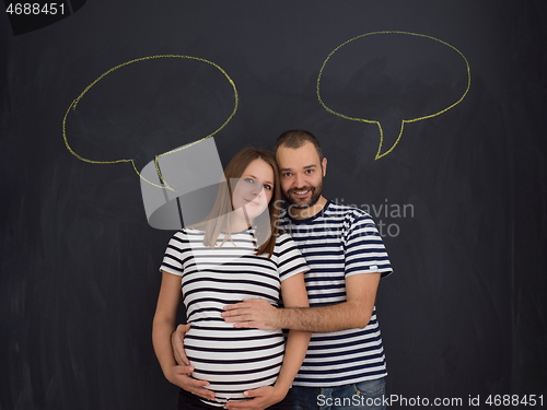 Image of pregnant couple posing against black chalk drawing board