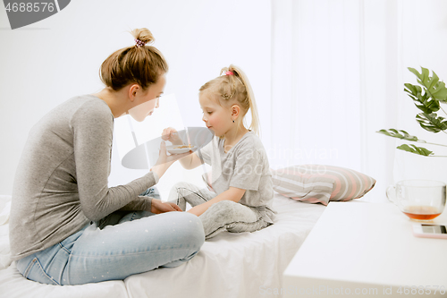 Image of Young mother and her little daughter hugging and kissing on bed