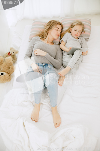 Image of Young mother and her little daughter hugging and kissing on bed