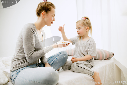 Image of Young mother and her little daughter hugging and kissing on bed