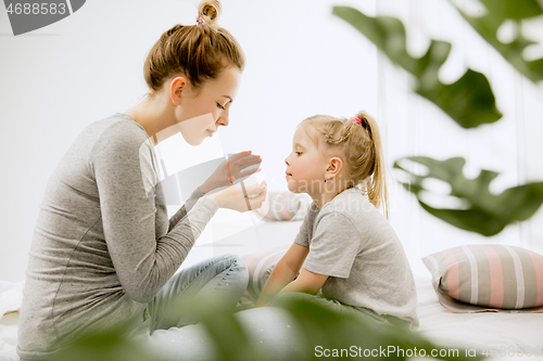 Image of Young mother and her little daughter hugging and kissing on bed