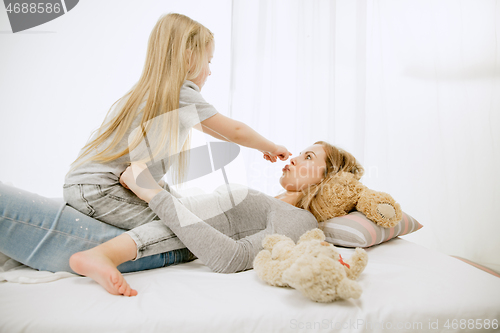 Image of Young mother and her little daughter hugging and kissing on bed