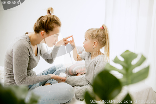 Image of Young mother and her little daughter hugging and kissing on bed