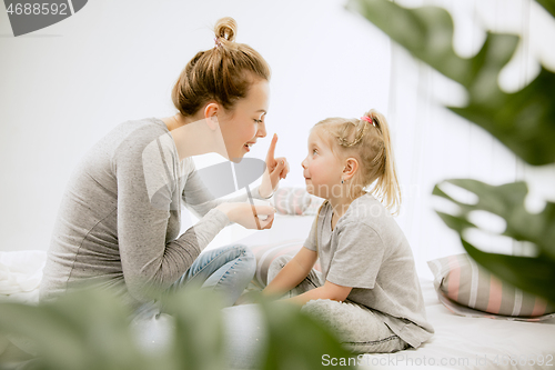 Image of Young mother and her little daughter hugging and kissing on bed