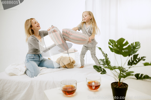 Image of Young mother and her little daughter hugging and kissing on bed