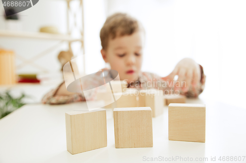 Image of Little child sitting on the floor. Pretty boy palying with wooden cubes at home