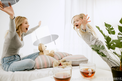 Image of Young mother and her little daughter hugging and kissing on bed