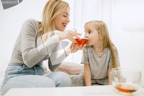 Image of Young mother and her little daughter hugging and kissing on bed