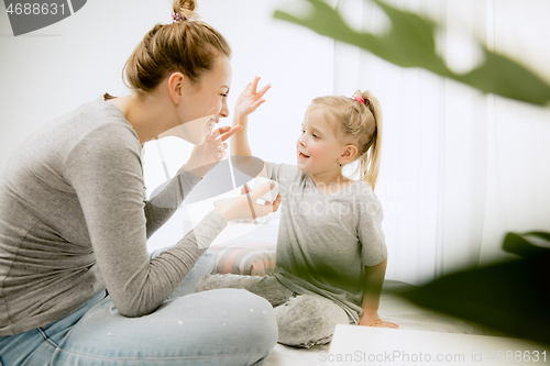 Image of Young mother and her little daughter hugging and kissing on bed