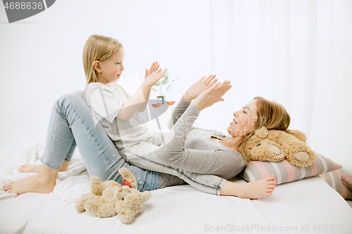 Image of Young mother and her little daughter hugging and kissing on bed