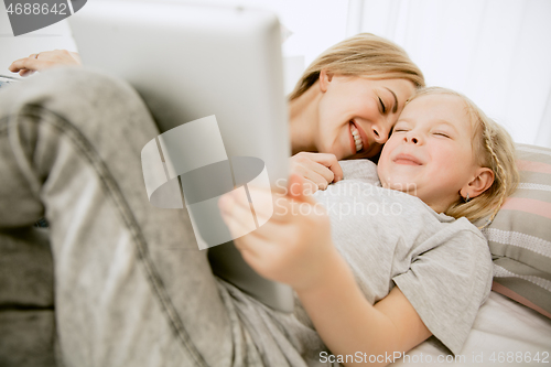 Image of Young mother and her little daughter hugging and kissing on bed