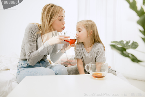 Image of Young mother and her little daughter hugging and kissing on bed