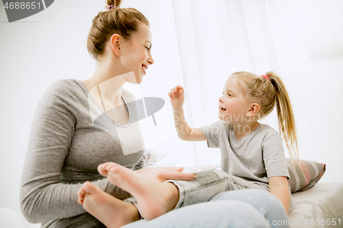 Image of Young mother and her little daughter hugging and kissing on bed