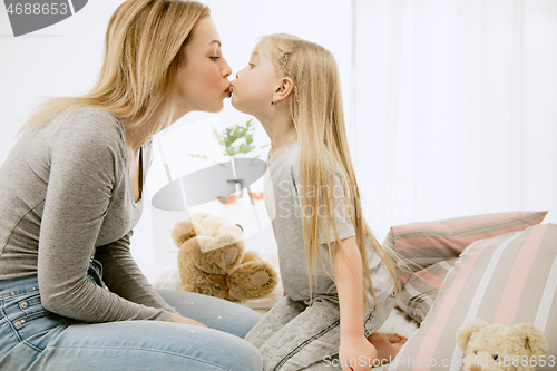 Image of Young mother and her little daughter hugging and kissing on bed