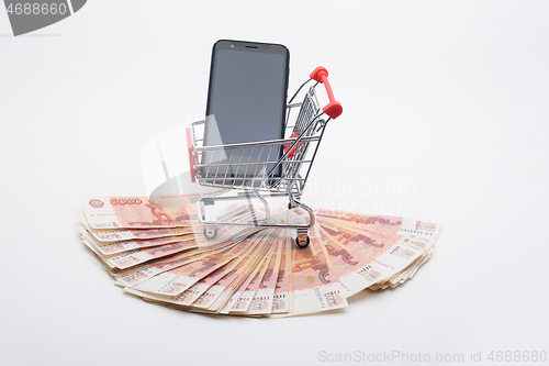 Image of Against the background of five thousandth bills, there is a grocery cart with a phone