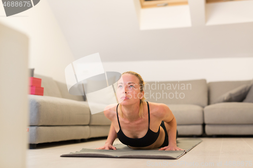 Image of Beautiful blonde woman doing home workout indoors. Woman practice yoga at home. Fit girl using workout tutorials for healthy active lifestyle. Woman using quarantine for home workouts.