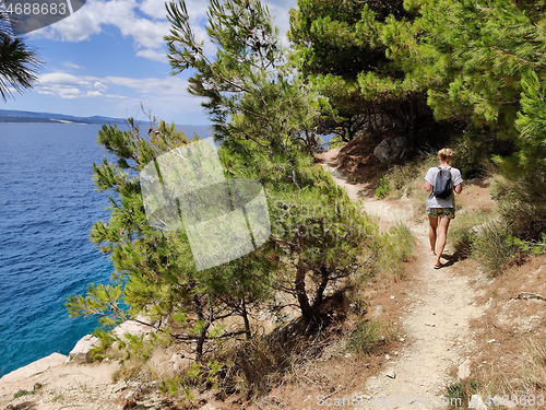 Image of Young active feamle tourist wearing small backpack walking on coastal path among pine trees looking for remote cove to swim alone in peace on seaside in Croatia. Travel and adventure concept