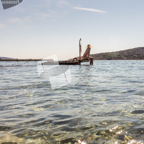 Image of View of unrecognizable woman wearing big summer sun hat tanning topless and relaxing on old wooden pier in remote calm cove of Adriatic sea, Croatia