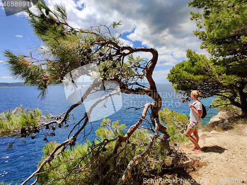 Image of Young active feamle tourist wearing small backpack walking on coastal path among pine trees looking for remote cove to swim alone in peace on seaside in Croatia. Travel and adventure concept