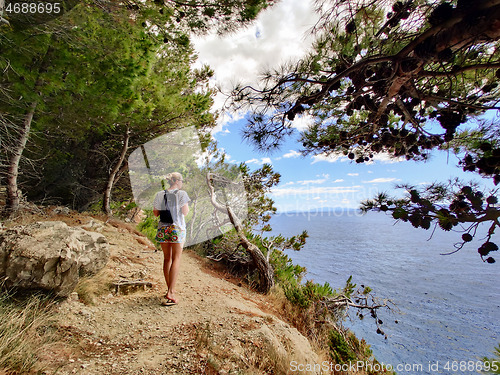 Image of Young active feamle tourist wearing small backpack walking on coastal path among pine trees looking for remote cove to swim alone in peace on seaside in Croatia. Travel and adventure concept