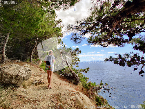 Image of Young active feamle tourist wearing small backpack walking on coastal path among pine trees looking for remote cove to swim alone in peace on seaside in Croatia. Travel and adventure concept