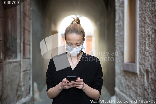 Image of COVID-19 pandemic coronavirus. Casual caucasian woman at medieval city street using mobile phone, wearing protective face mask against spreading of coronavirus and disease transmission