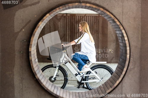 Image of Casual caucasian teenager riding urban electric bicycle in urban environment. Urban mobility concept