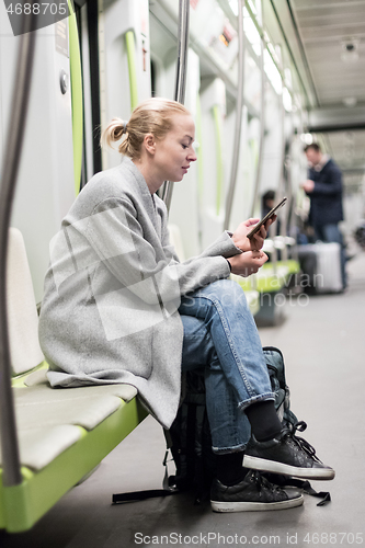 Image of Portrait of lovely girl typing message on mobile phone in almost empty public subway train. Staying at home and social distancing recomented due to corona virus pandemic outbreak