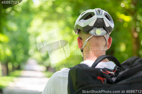 Image of Rear view of unrecognizable man wearing protective helmet on bicycle cycling in city park