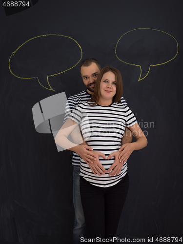 Image of pregnant couple posing against black chalk drawing board