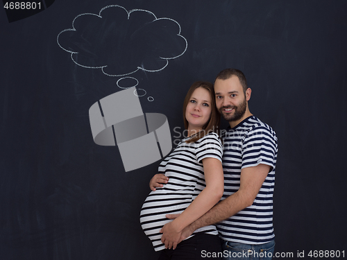 Image of pregnant couple posing against black chalk drawing board