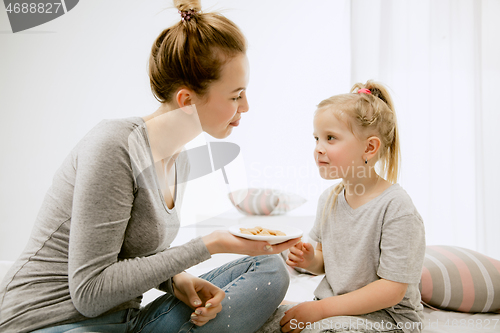 Image of Young mother and her little daughter hugging and kissing on bed